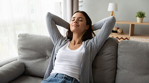 woman relaxing on the couch with her eyes closed and hands behind her head
